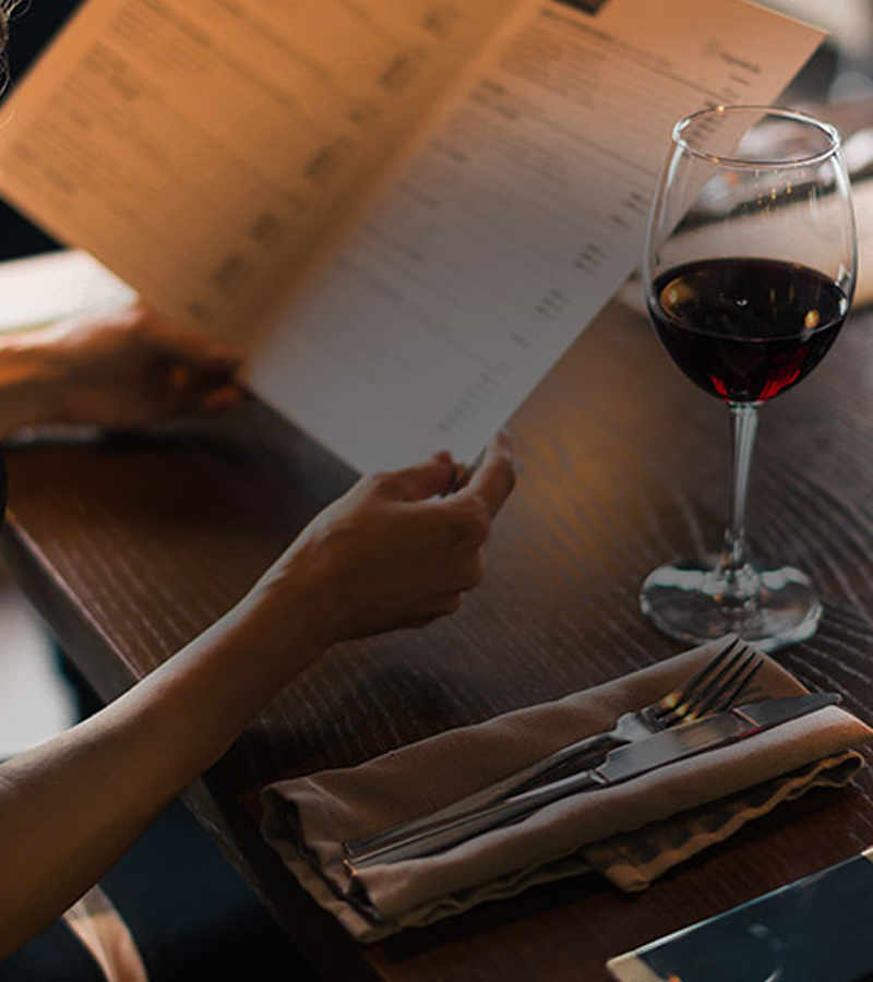 Kvinde kigger på en menu ed et glas rødvin