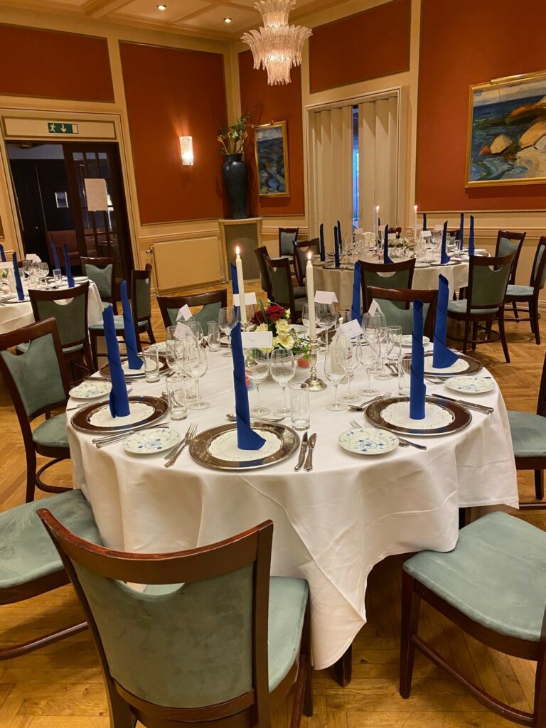Runde borde i sal, opdækket med hvide due, Royal Copenhagen service, høje lys og blå servietter